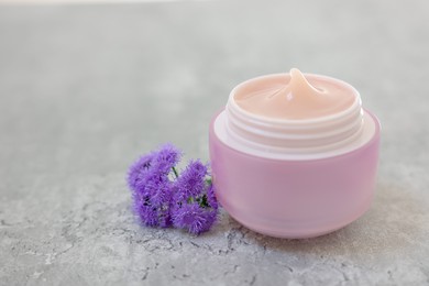 Photo of Jar of cream and ageratum flowers on gray table, closeup. Space for text