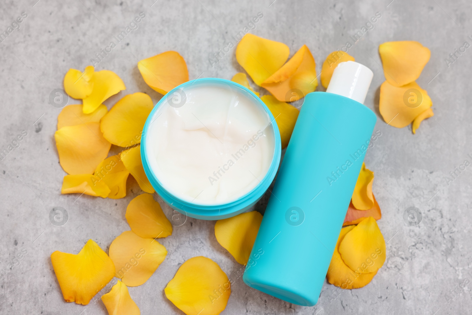 Photo of Cosmetic products and yellow petals on gray table, above view