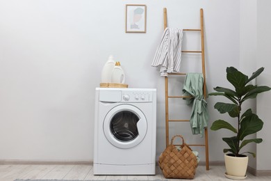 Photo of Washing machine, detergents, houseplant and ladder in laundry room, space for text