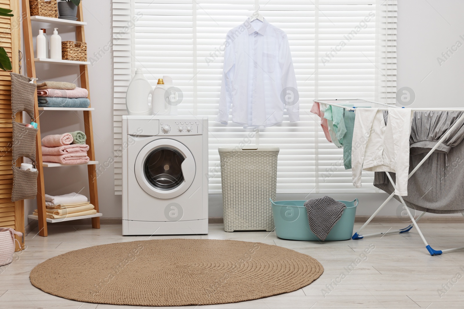 Photo of Washing machine, detergents, towels, baskets and drying rack in laundry room