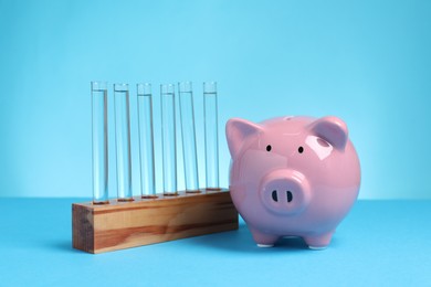 Photo of Water save concept. Piggy bank and liquid in test tubes on light blue background