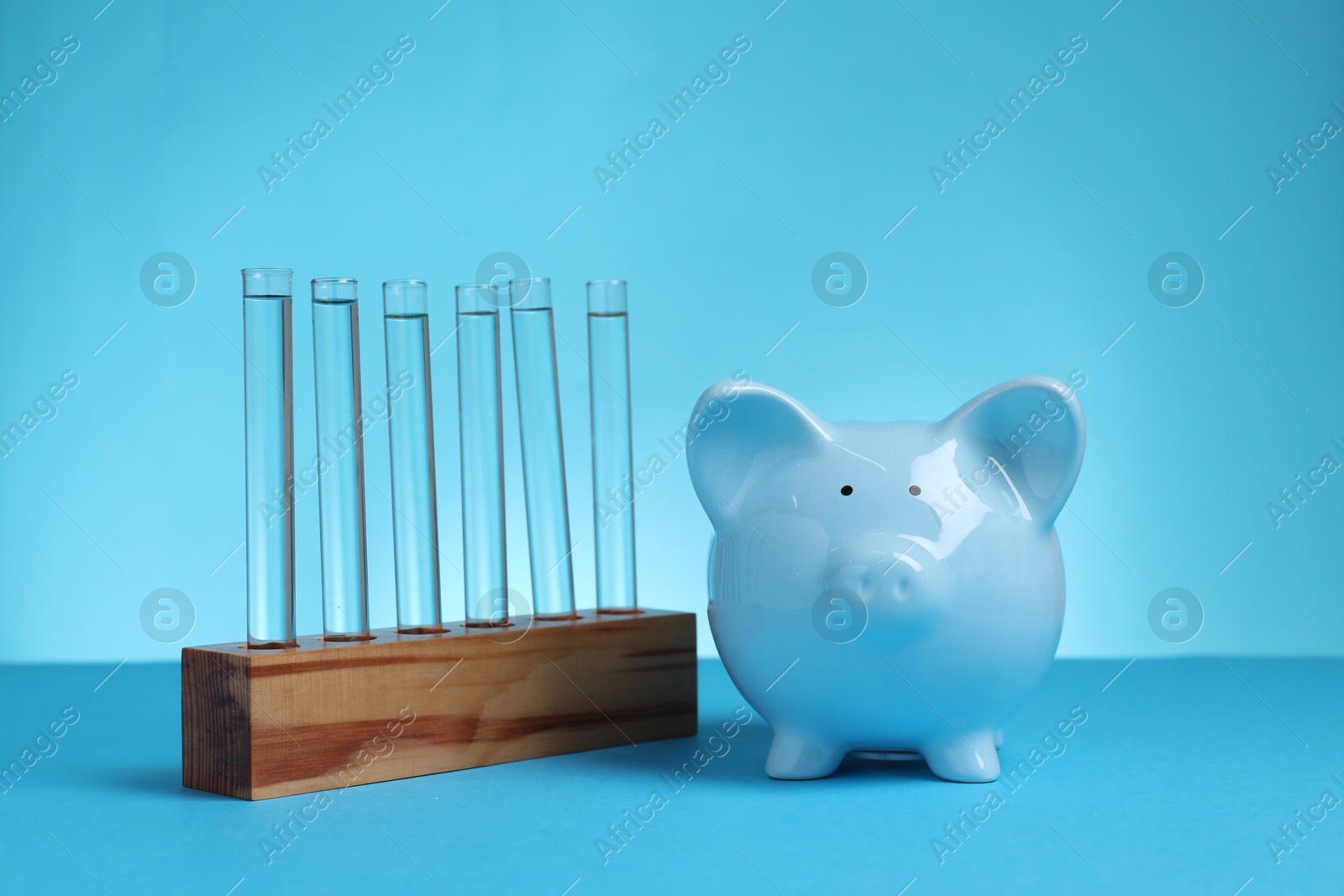 Photo of Water save concept. Piggy bank and liquid in test tubes on light blue background