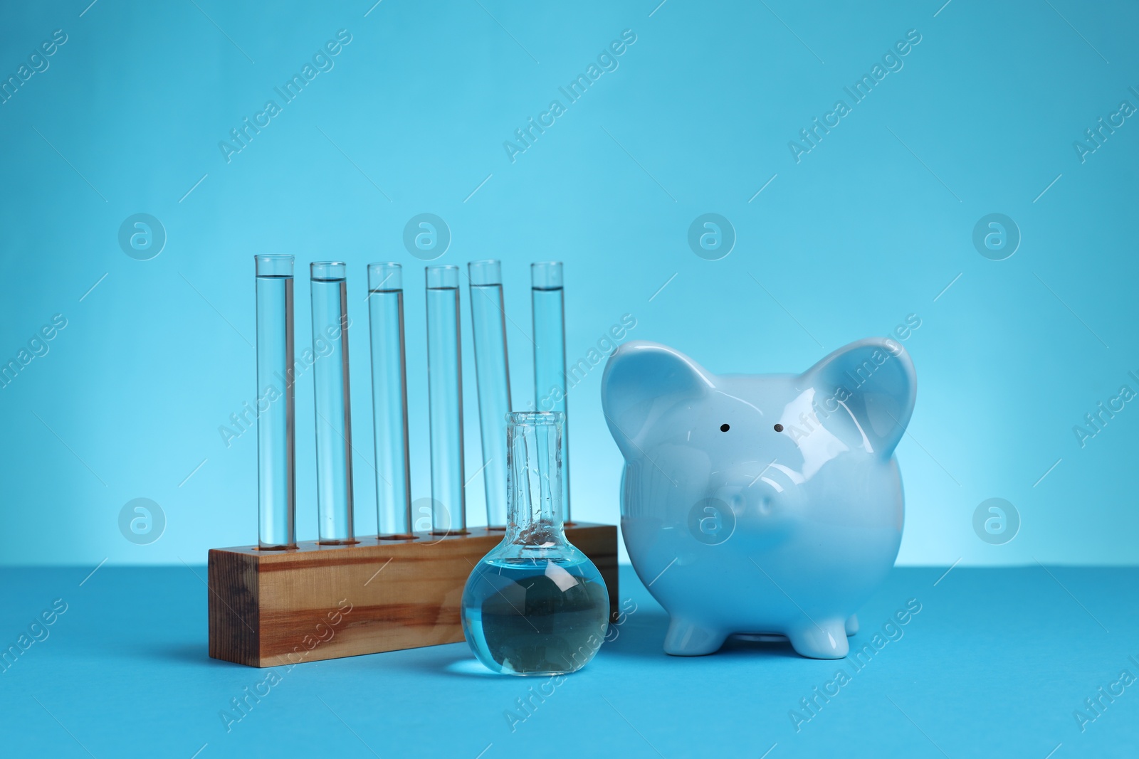 Photo of Water save concept. Piggy bank, laboratory flask and test tubes with liquid on light blue background