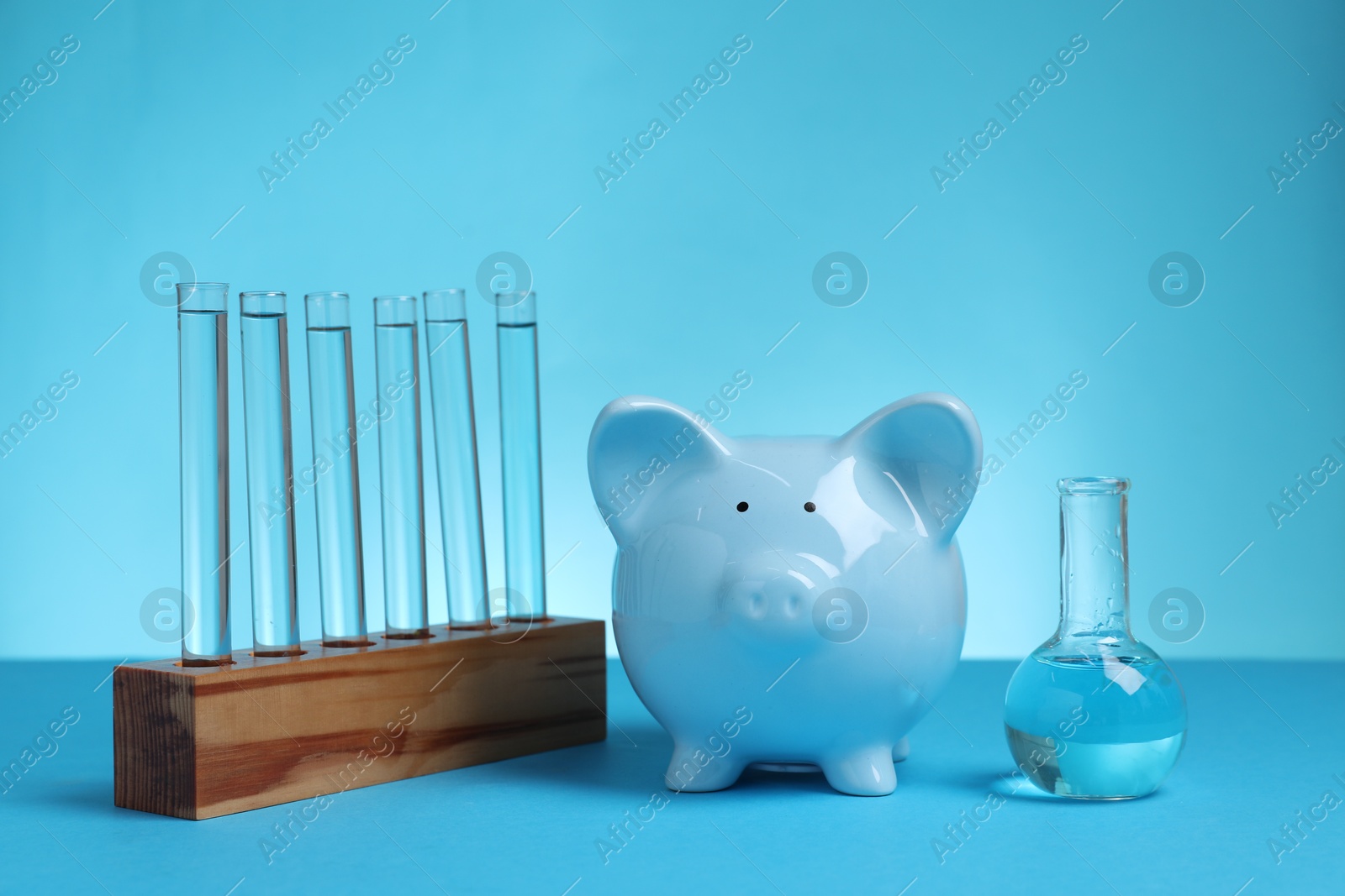 Photo of Water save concept. Piggy bank, laboratory flask and test tubes with liquid on light blue background
