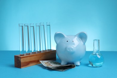 Photo of Water save concept. Piggy bank, dollar banknotes laboratory flask and test tubes with liquid on light blue background