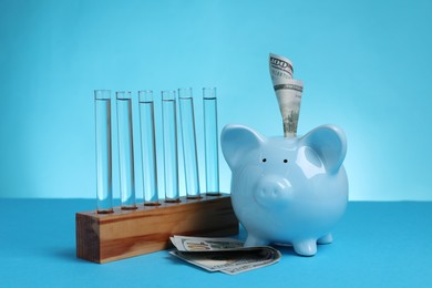 Photo of Water save concept. Piggy bank, dollar banknotes and liquid in test tubes on light blue background