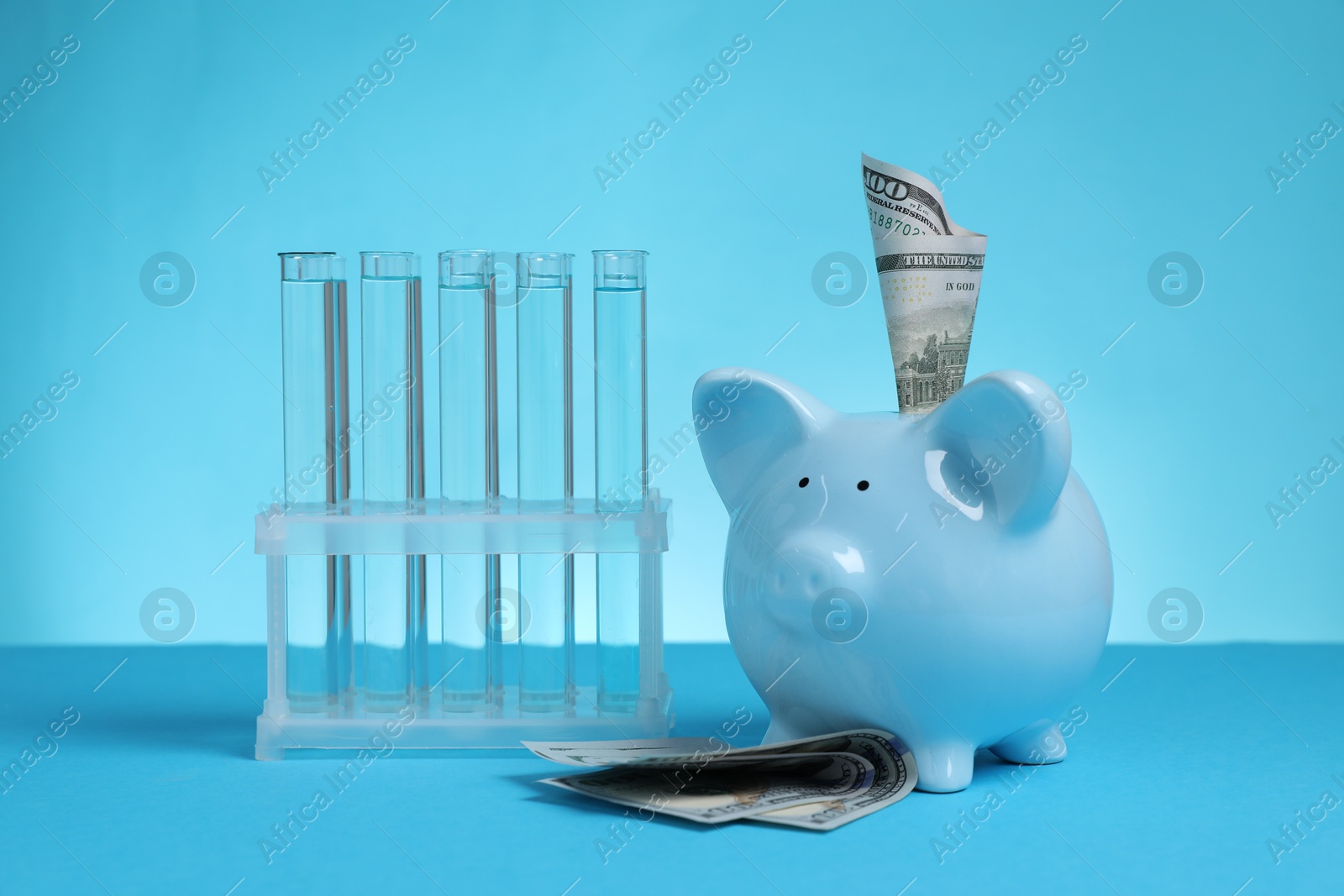Water save concept. Piggy bank, dollar banknotes and liquid in test tubes on light blue background Photo of Water save concept. Piggy bank, dollar banknotes and liquid in test tubes on light blue background