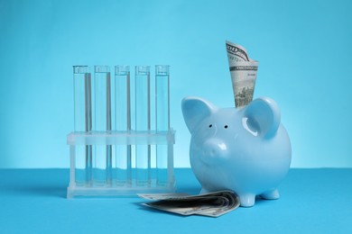 Photo of Water save concept. Piggy bank, dollar banknotes and liquid in test tubes on light blue background