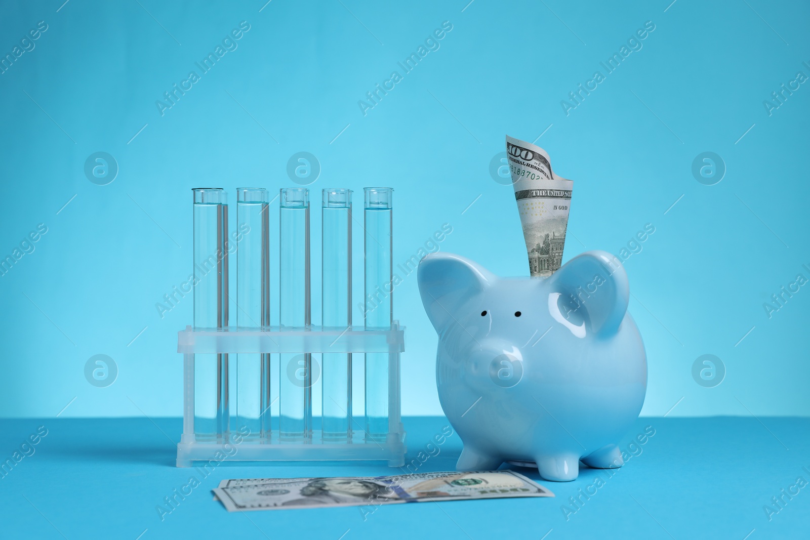 Photo of Water save concept. Piggy bank, dollar banknotes and liquid in test tubes on light blue background