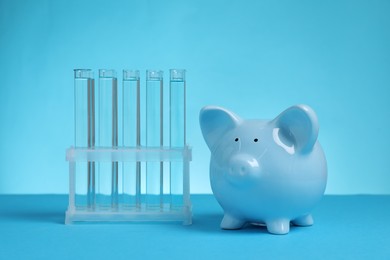 Photo of Water save concept. Piggy bank and liquid in test tubes on light blue background