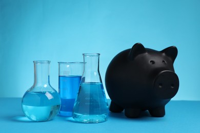 Photo of Water save concept. Piggy bank and laboratory glassware with liquid on light blue background