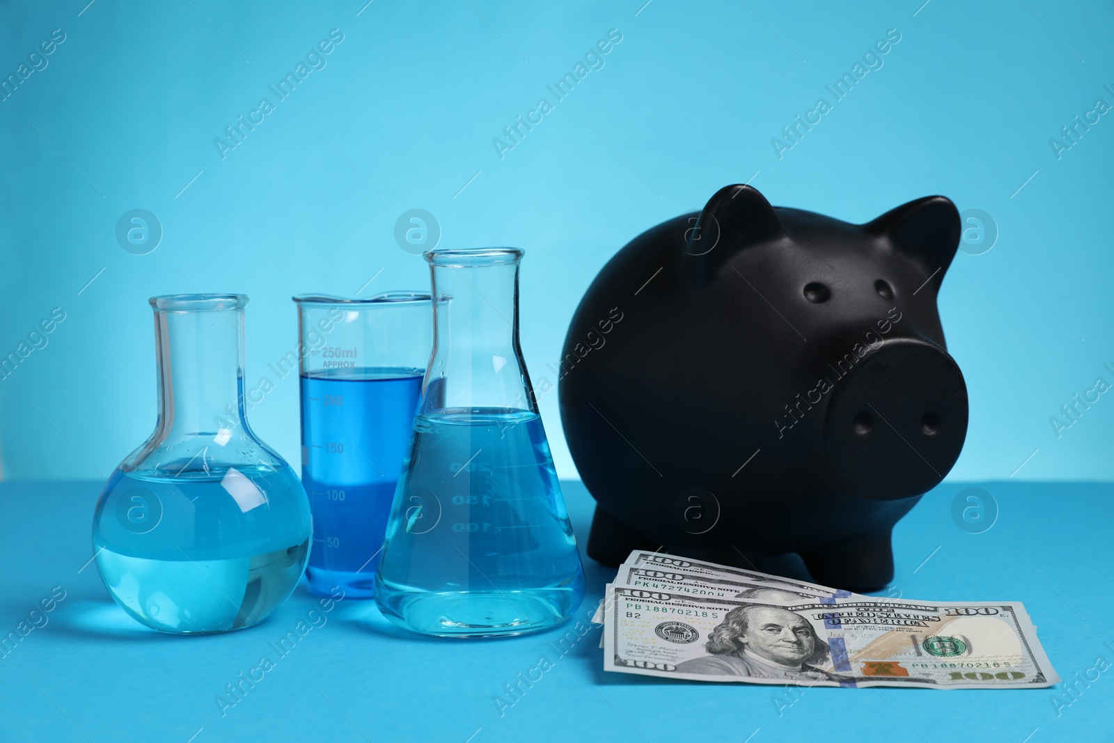 Water save concept. Piggy bank, dollar banknotes and laboratory glassware with liquid on light blue background Photo of Water save concept. Piggy bank, dollar banknotes and laboratory glassware with liquid on light blue background
