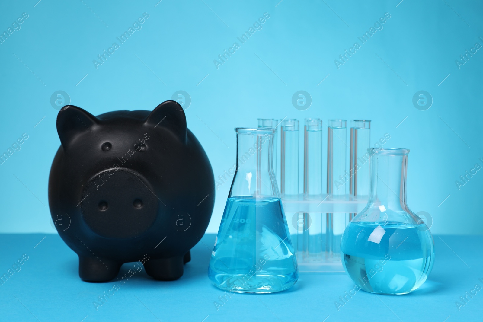 Photo of Water save concept. Piggy bank and different laboratory glassware with liquid on light blue background