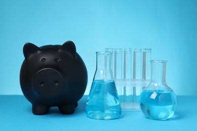 Photo of Water save concept. Piggy bank and different laboratory glassware with liquid on light blue background