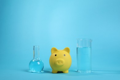 Photo of Water save concept. Piggy bank and laboratory glassware with liquid on light blue background