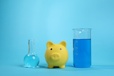 Photo of Water save concept. Piggy bank and laboratory glassware with liquid on light blue background