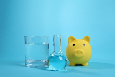 Photo of Water save concept. Piggy bank and laboratory glassware with liquid on light blue background