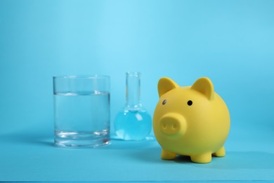 Photo of Water save concept. Piggy bank and laboratory glassware with liquid on light blue background