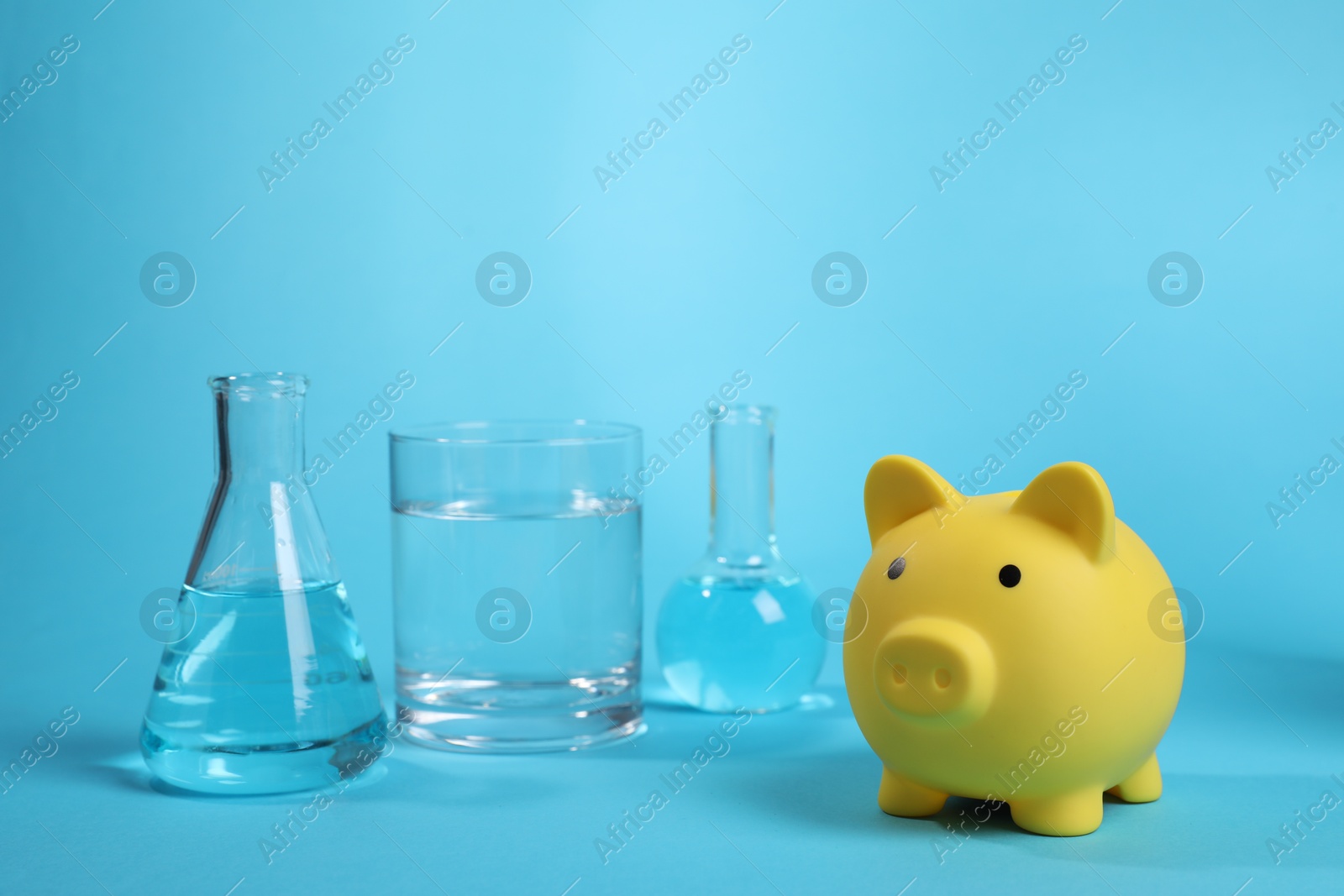 Photo of Water save concept. Piggy bank and laboratory glassware with liquid on light blue background
