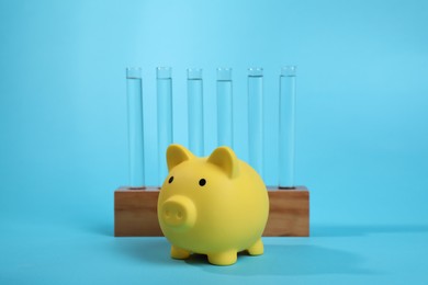 Photo of Water save concept. Piggy bank and liquid in test tubes on light blue background