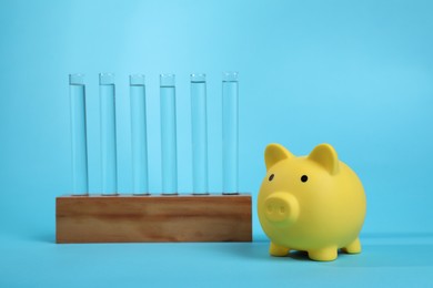 Photo of Water save concept. Piggy bank and liquid in test tubes on light blue background