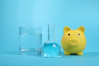 Photo of Water save concept. Piggy bank and laboratory glassware with liquid on light blue background