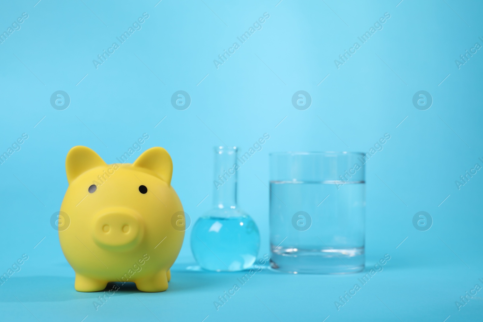 Photo of Water save concept. Piggy bank and laboratory glassware with liquid on light blue background