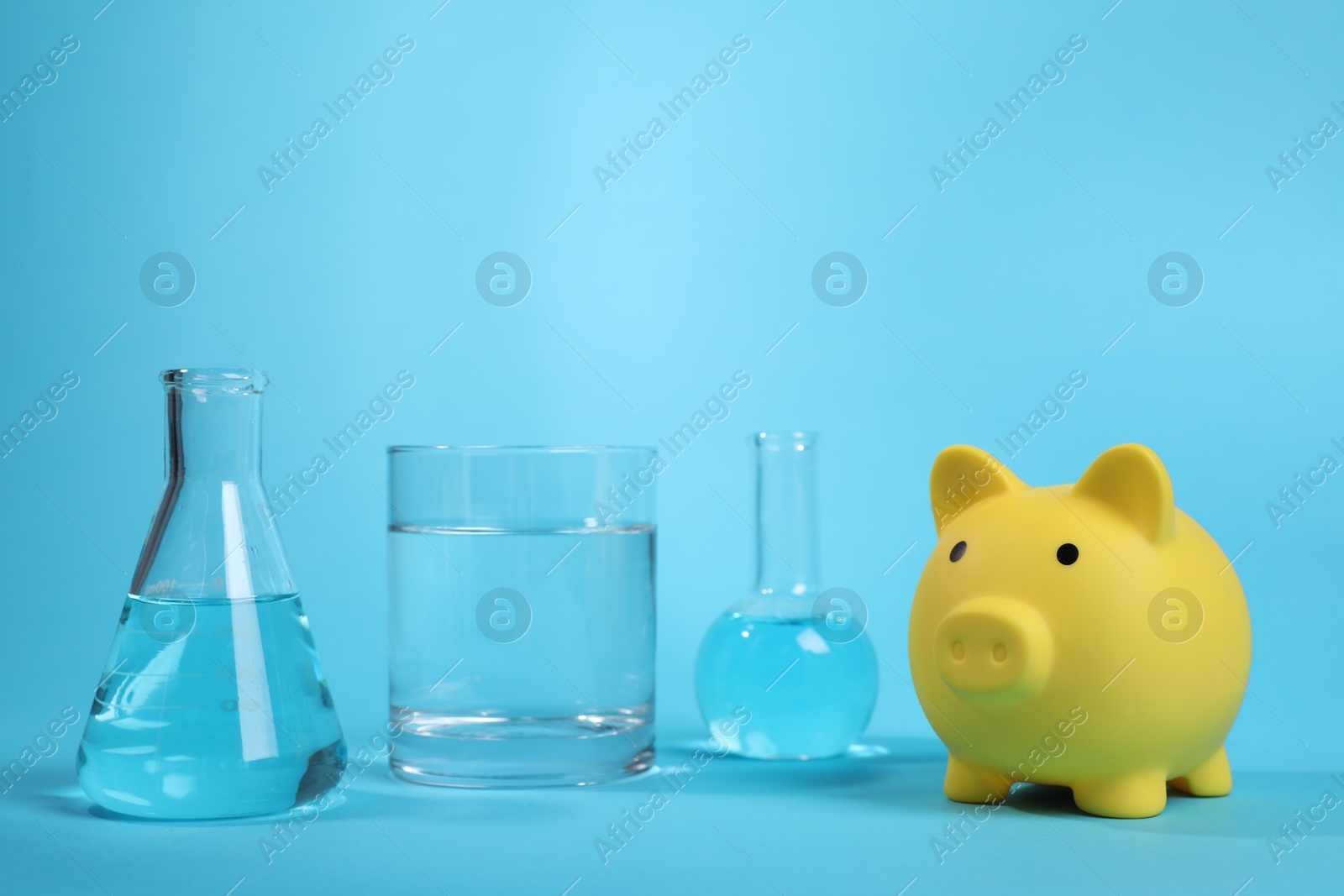 Photo of Water save concept. Piggy bank and laboratory glassware with liquid on light blue background