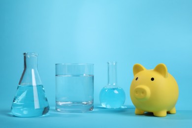 Photo of Water save concept. Piggy bank and laboratory glassware with liquid on light blue background