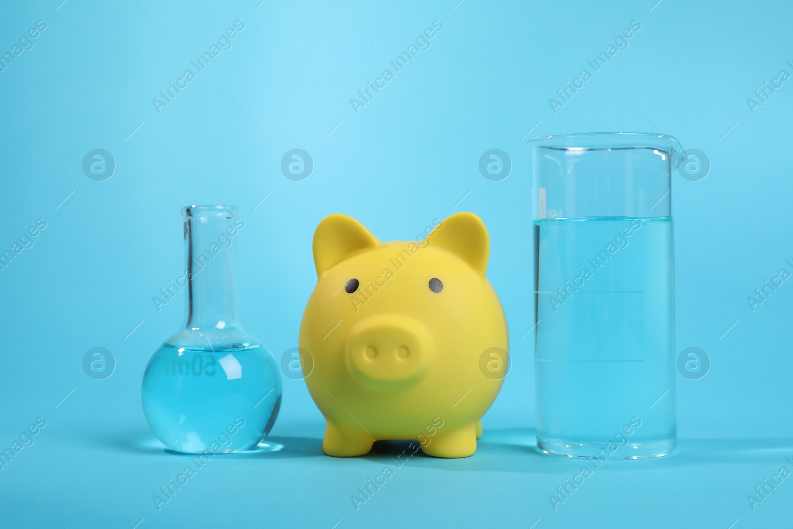 Photo of Water save concept. Piggy bank and laboratory glassware with liquid on light blue background