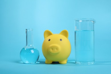 Photo of Water save concept. Piggy bank and laboratory glassware with liquid on light blue background