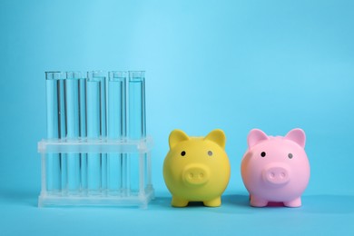 Photo of Water save concept. Piggy banks and liquid in test tubes on light blue background