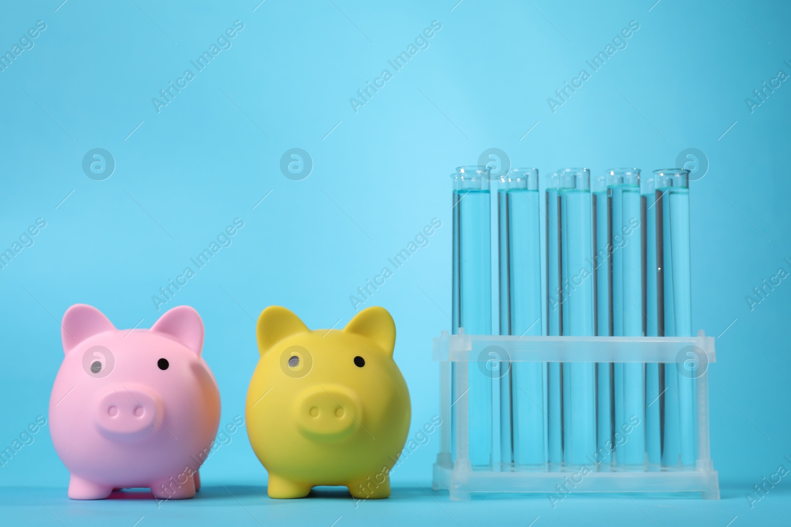 Water save concept. Piggy banks and liquid in test tubes on light blue background Photo of Water save concept. Piggy banks and liquid in test tubes on light blue background