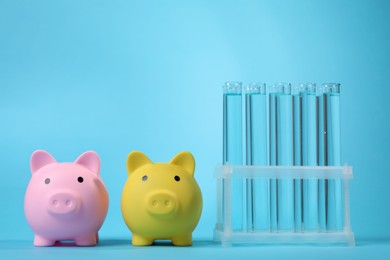 Photo of Water save concept. Piggy banks and liquid in test tubes on light blue background