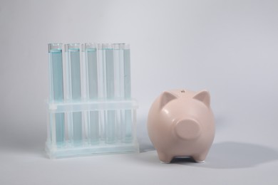 Photo of Water save concept. Piggy bank and liquid in test tubes on light grey background