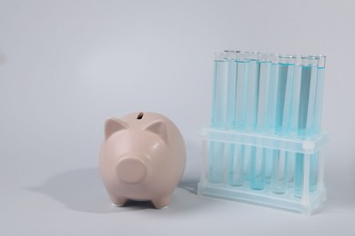 Photo of Water save concept. Piggy bank and liquid in test tubes on light grey background