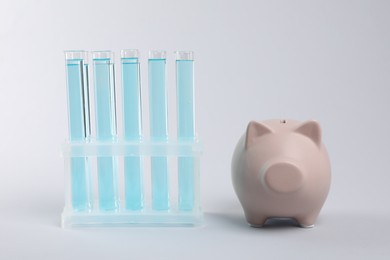 Photo of Water save concept. Piggy bank and liquid in test tubes on light grey background