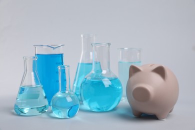 Photo of Water save concept. Piggy bank and laboratory glassware with liquid on light grey background