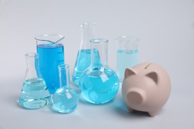 Photo of Water save concept. Piggy bank and laboratory glassware with liquid on light grey background