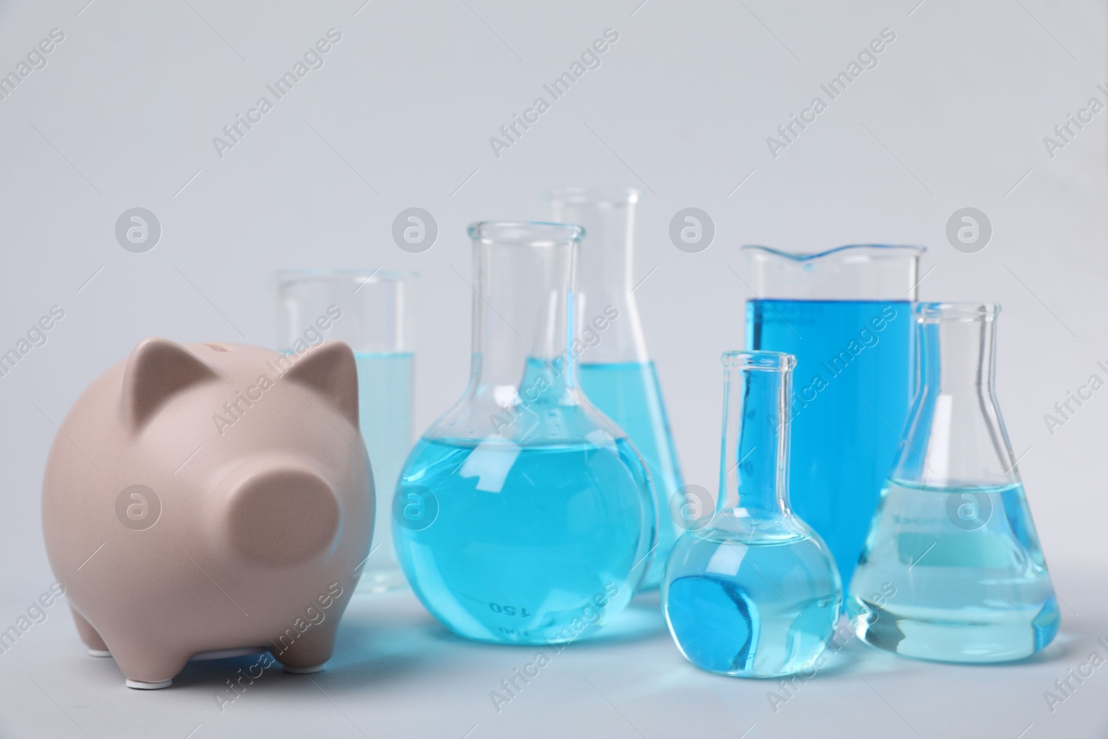 Photo of Water save concept. Piggy bank and laboratory glassware with liquid on light grey background