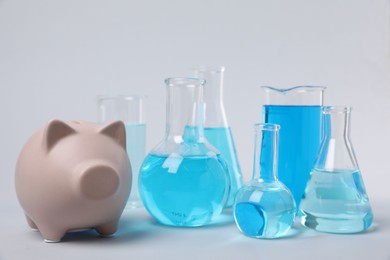 Water save concept. Piggy bank and laboratory glassware with liquid on light grey background