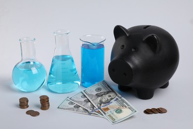 Photo of Water save concept. Piggy bank, money and laboratory glassware with liquid on light grey background