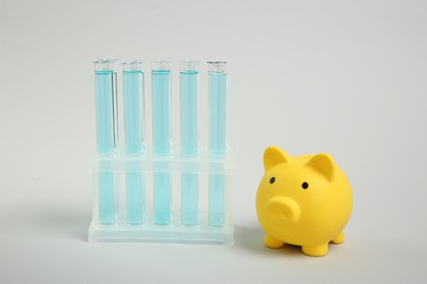 Photo of Water save concept. Piggy bank and liquid in test tubes on light grey background