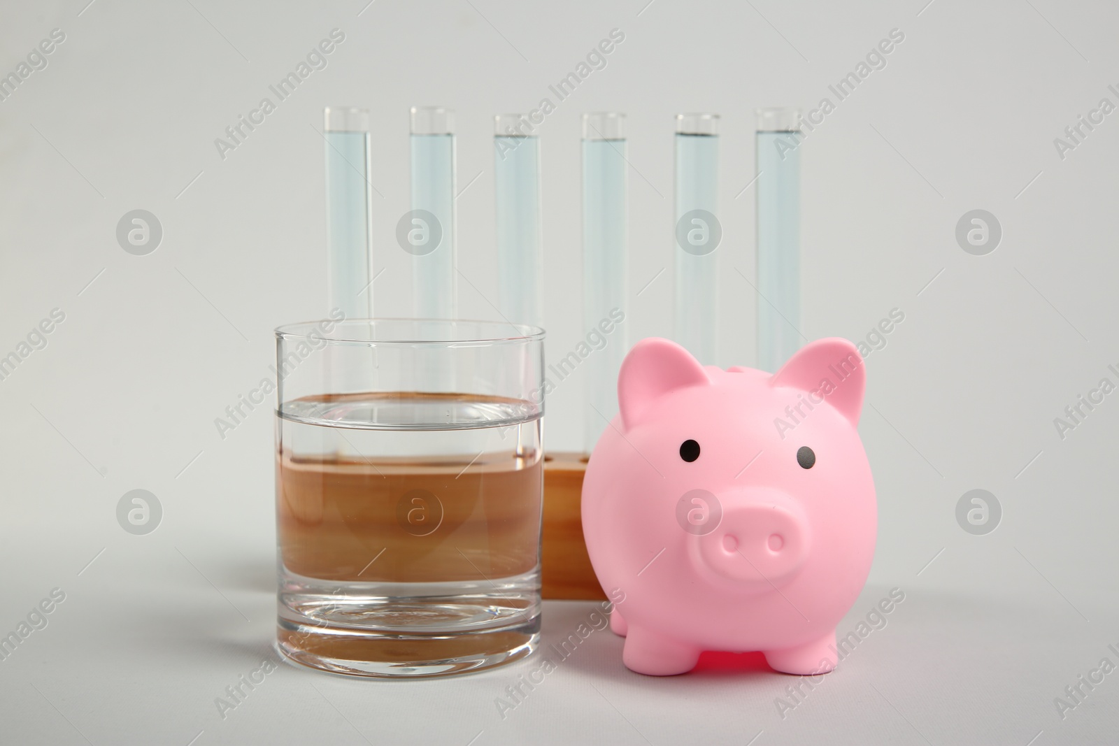 Photo of Water save concept. Piggy bank, test tubes and glass with liquid on light grey background