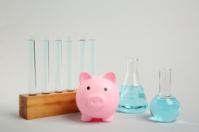 Water save concept. Piggy bank and different laboratory glassware with liquid on light grey background