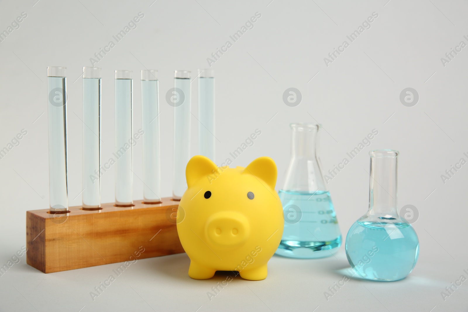 Photo of Water save concept. Piggy bank and different laboratory glassware with liquid on light grey background