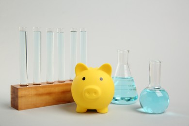 Photo of Water save concept. Piggy bank and different laboratory glassware with liquid on light grey background