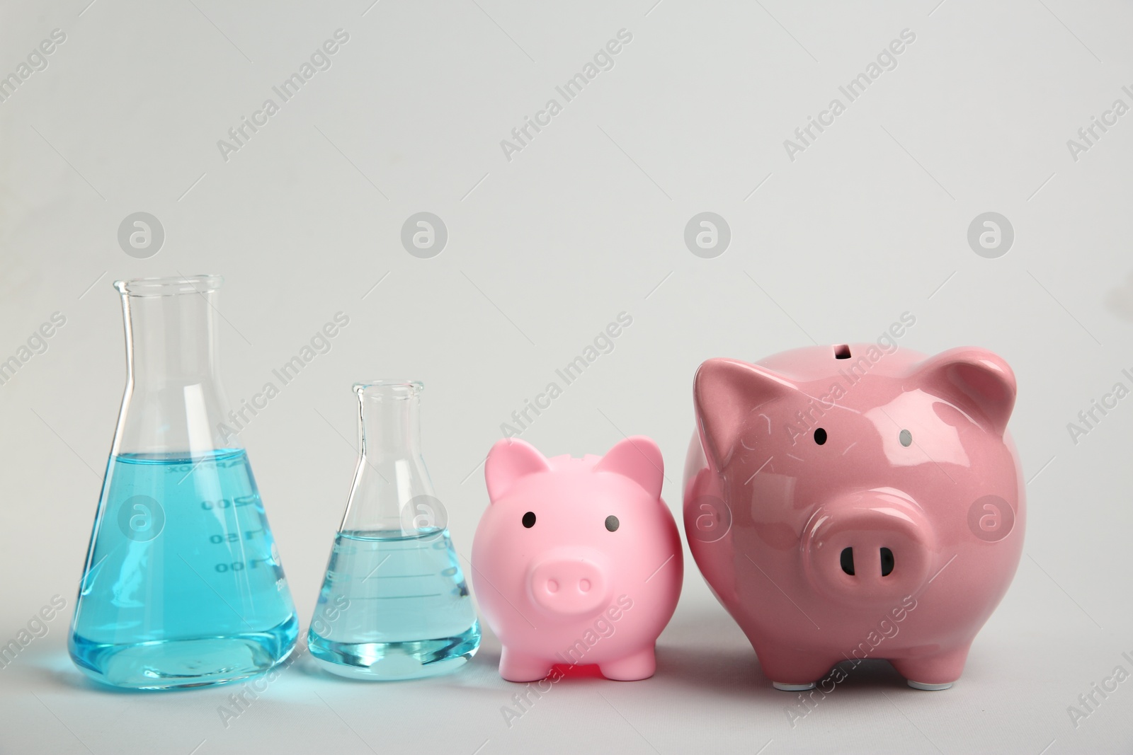 Photo of Water save concept. Piggy banks and laboratory glassware with liquid on light grey background