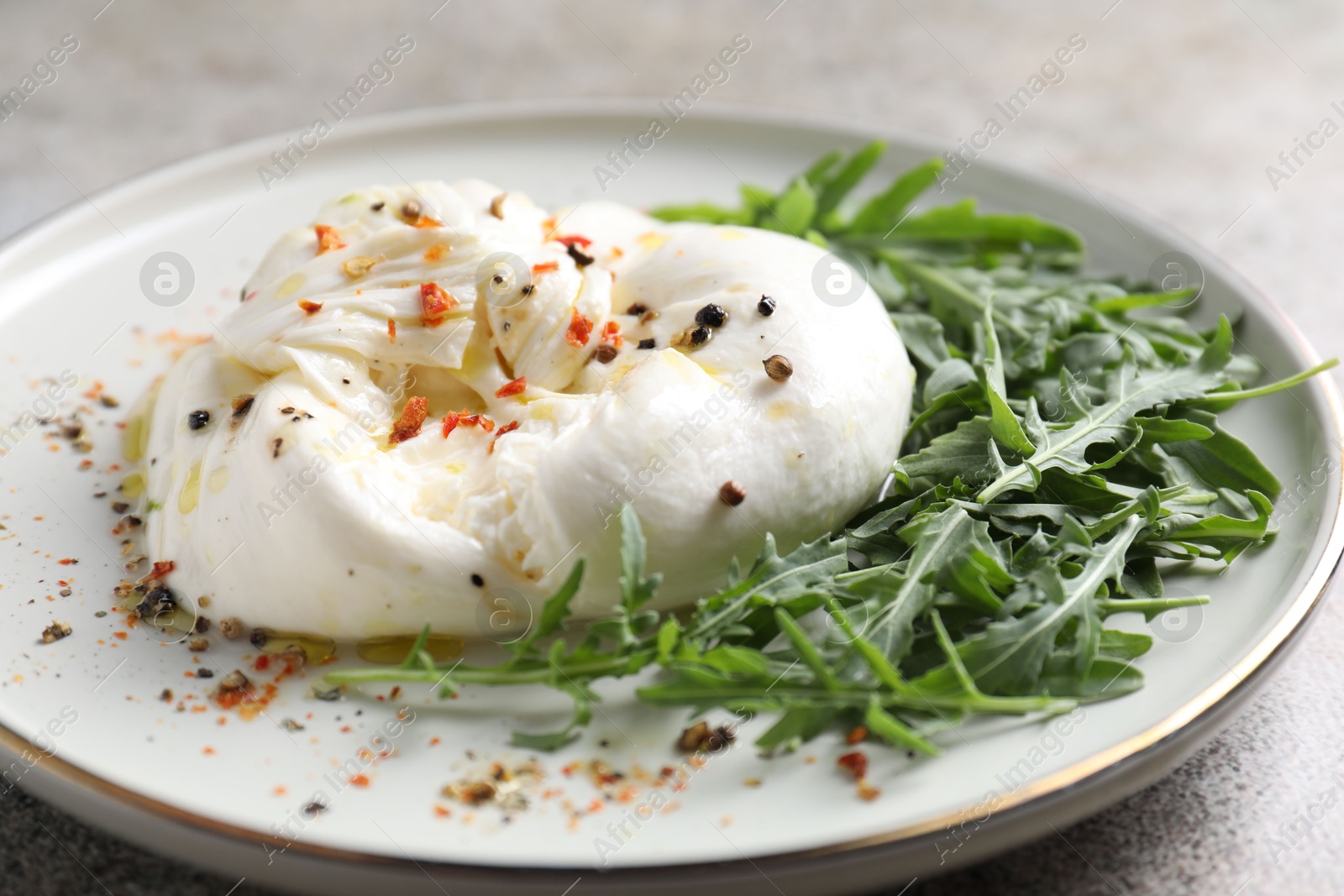 Photo of Delicious burrata cheese, arugula and spices on table, closeup