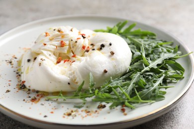 Delicious burrata cheese, arugula and spices on table, closeup